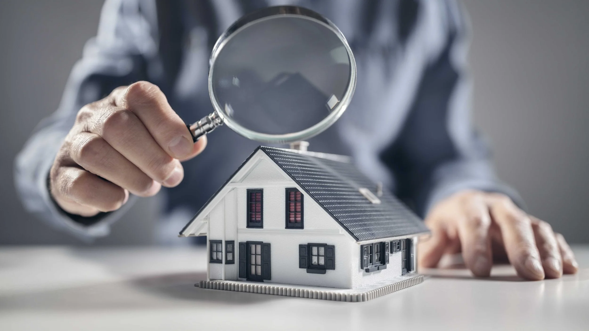 Magnifying glass held over a model house, representing a home inspection